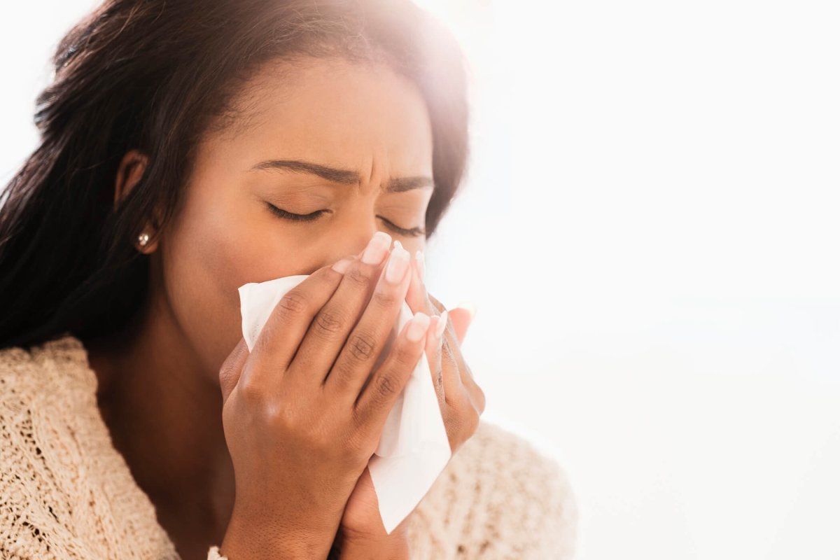 Woman wearing scarf coughing into her hand.